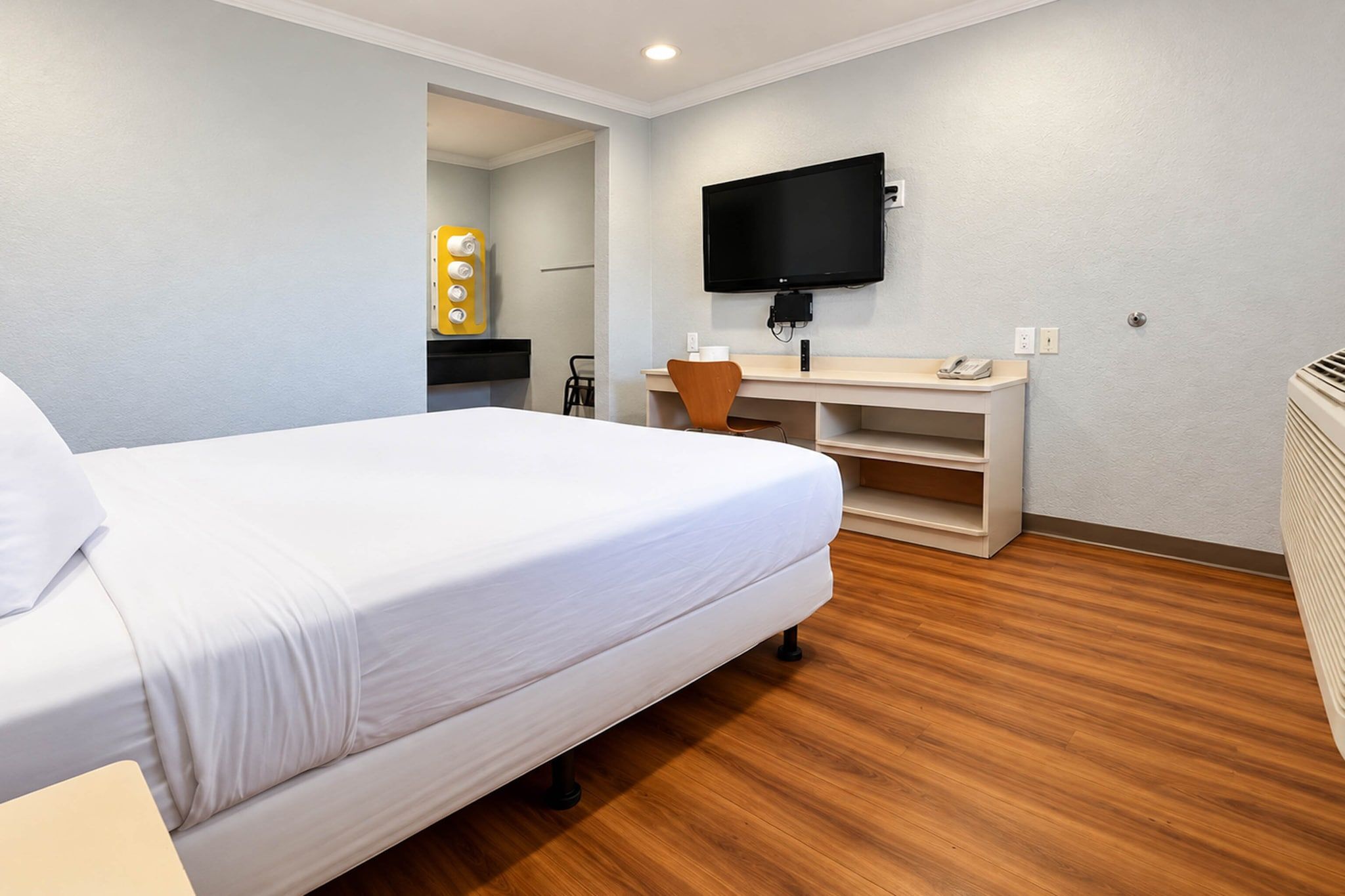 A hotel room with a bed, a desk, a chair, a flat-screen TV, and a heater.