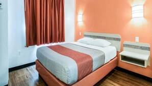Een hotelkamer met een bed, nachtkastje, raam met gordijnen en wandlampen.