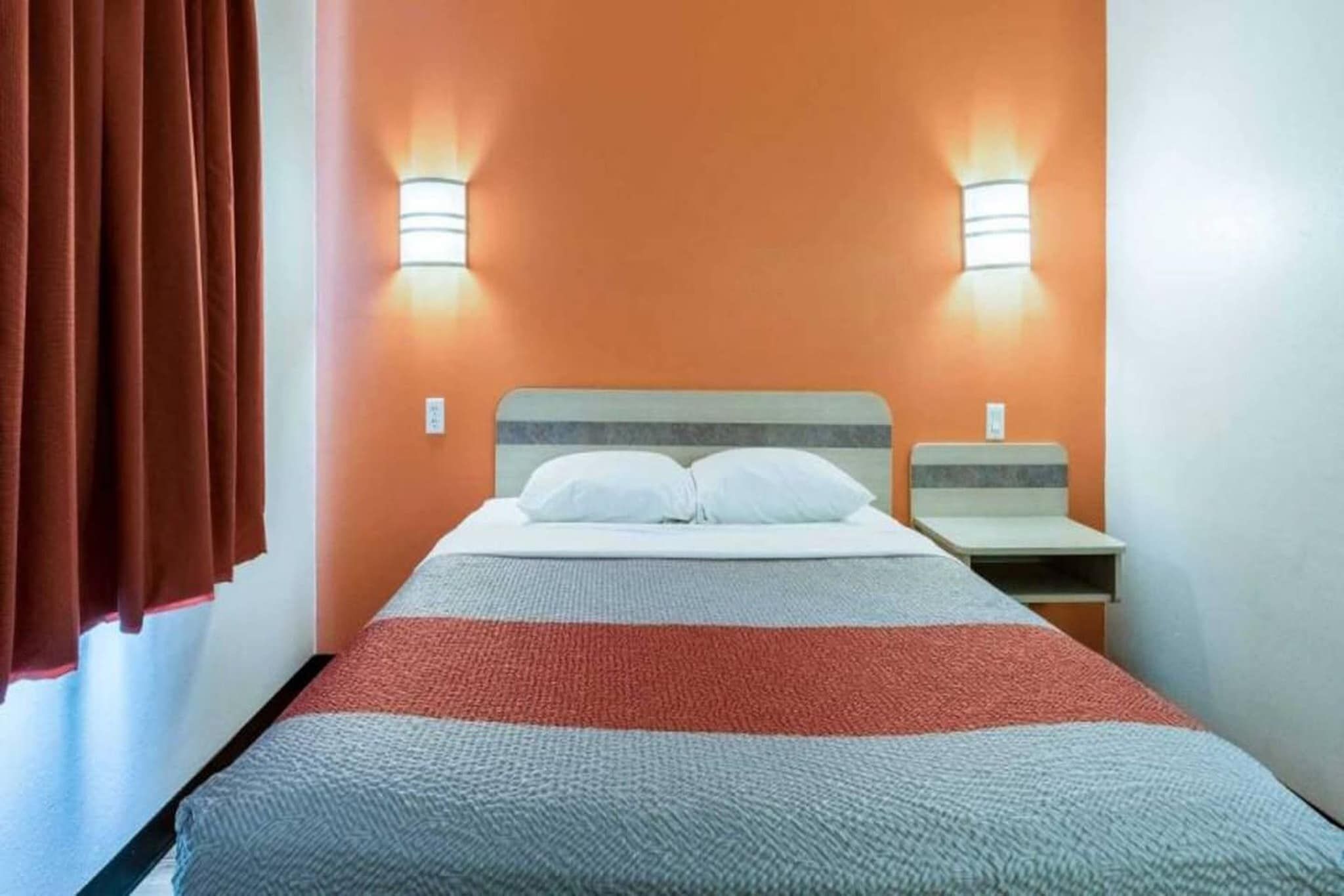 A hotel room with a bed, two bedside tables, and two wall-mounted lamps.