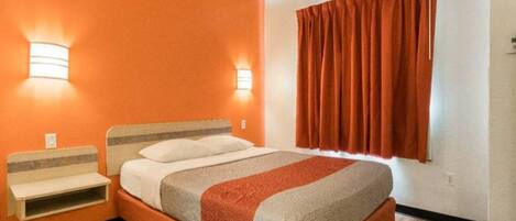 A hotel room with a bed, bedside tables, a window with curtains, and wall-mounted lights.