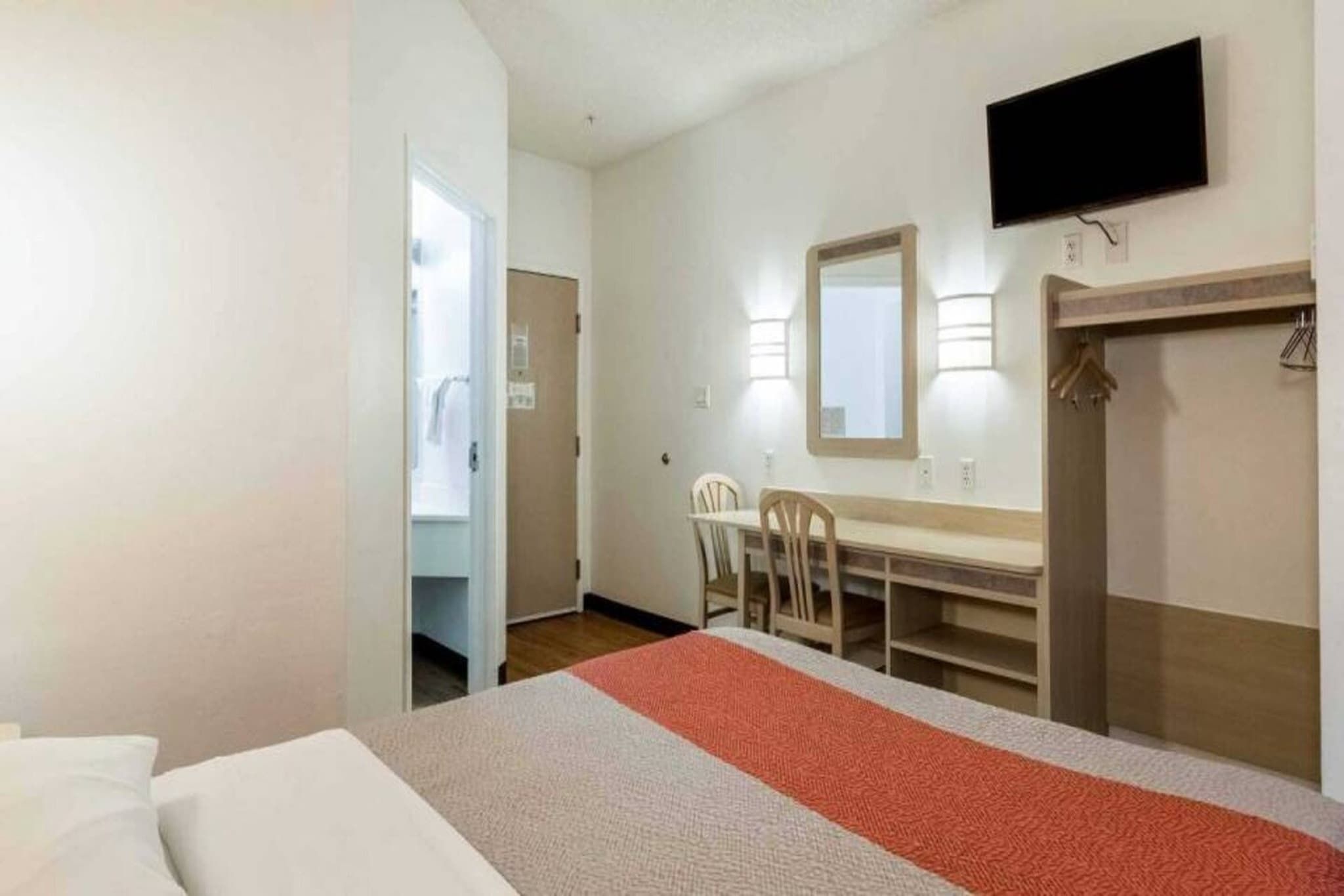 A hotel room with a bed, a desk with chairs, a television, and a wardrobe.