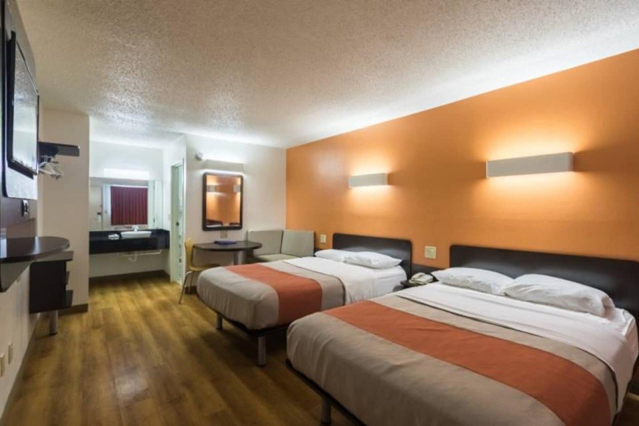 A hotel room with two beds, a desk, a mirror, and a bathroom.
