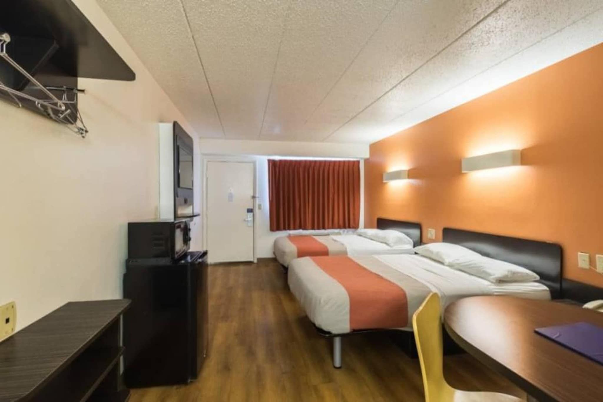 A hotel room with a bed, a desk, a chair, a TV, and a window with curtains.