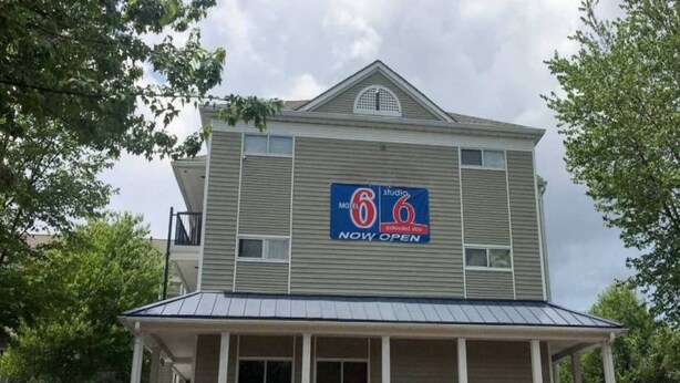 Een motel met twee verdiepingen en een blauw bord waarop staat dat het nu geopend is.