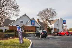 Un hôtel avec une enseigne indiquant le chiffre « 6 », une banderole annonçant « Nouvelles chambres » et un parking rempli de voitures.
