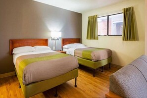 Une chambre d’hôtel avec deux lits, une table de chevet, une lampe et une fenêtre avec des rideaux.
