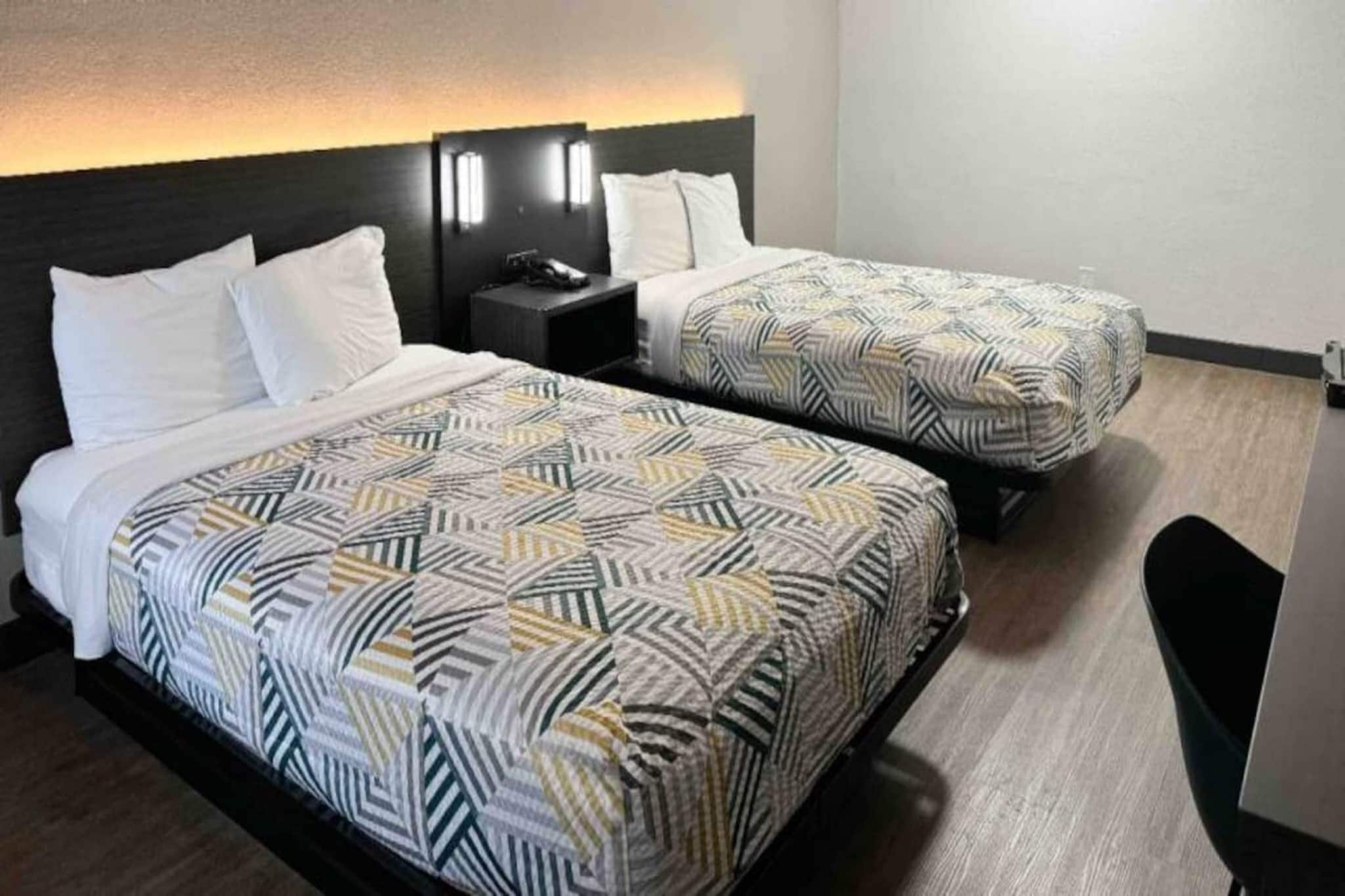 Une chambre d’h ôtel avec deux lits, chacun agrémenté de draps à motifs, une table de chevet et une lampe fixée au mur.