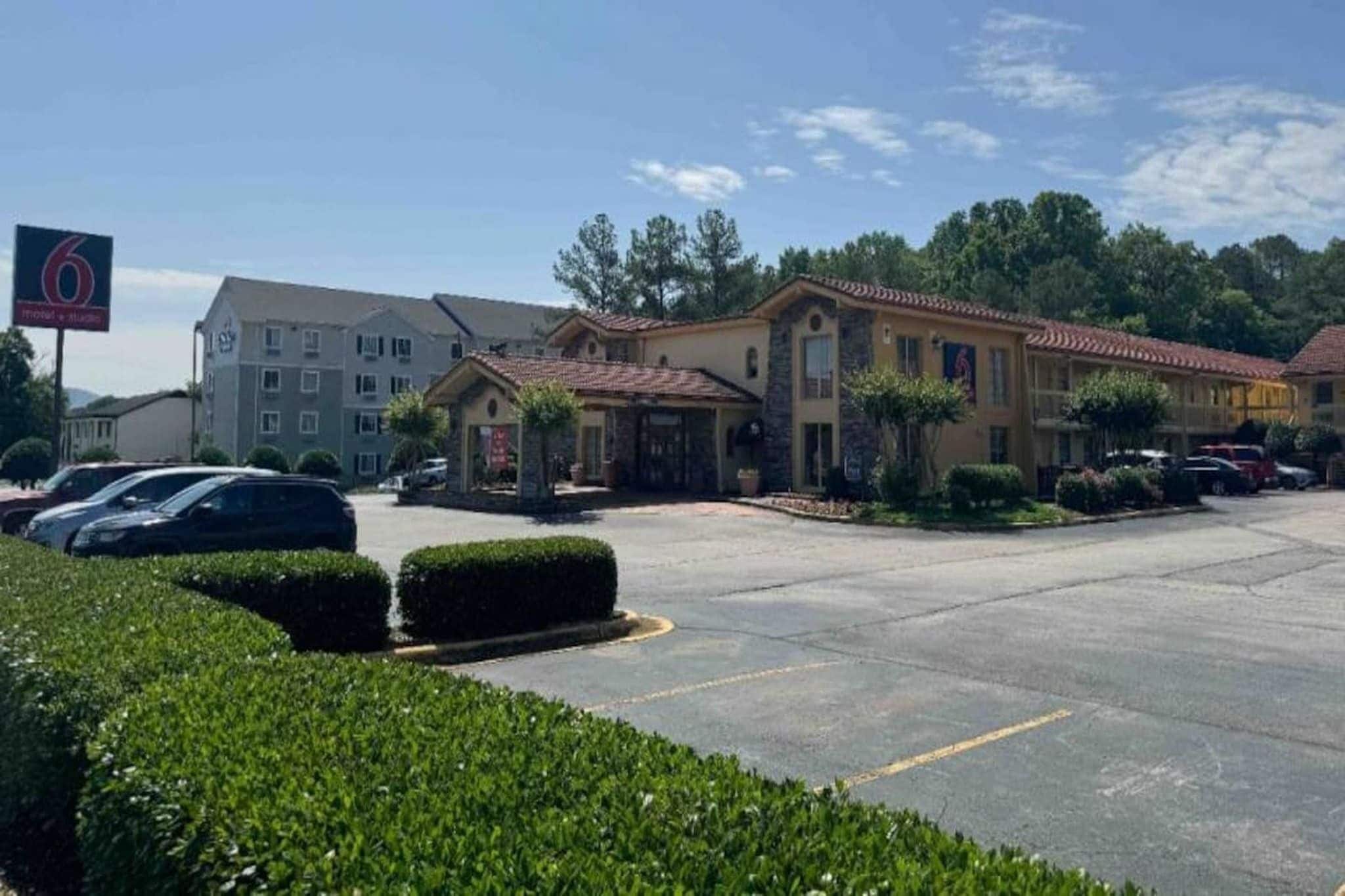 A hotel with a parking lot, a building with a red-tiled roof, and a sign with the number 6.