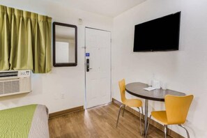 A hotel room with a bed, a desk with two chairs, a television, an air conditioning unit, and a door. - 1 Queen bed|Non-Smoking (Jacksonville)