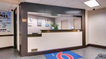 Zona de recepción de un hotel con mostrador, alfombra azul con logotipo y cartel con horario de atención.
