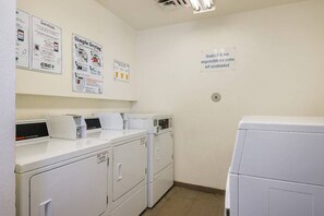 A laundry room with multiple washing machines and dryers, a wall-mounted bulletin board with various notices, and a sign stating Studio 6 is not responsible for unattended items. - 2 Queen Beds | Suite, Smoking (Greensboro)