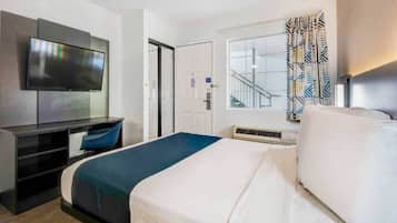 A hotel room with a bed, a desk with a chair, a television, a window with a view, and a door.