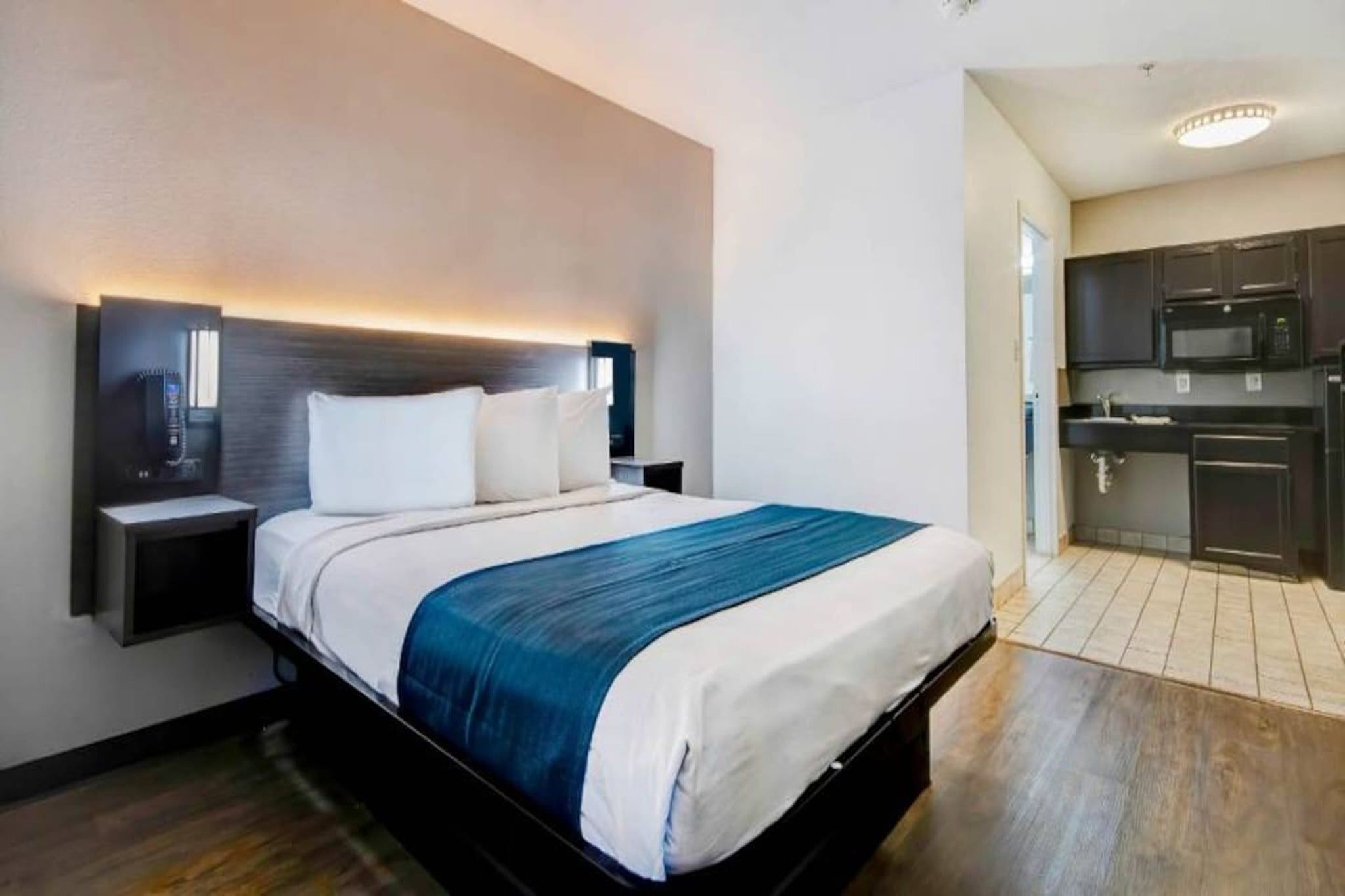 Habitación de hotel con cama, mesitas de noche, televisor integrado y una zona de kitchenette.