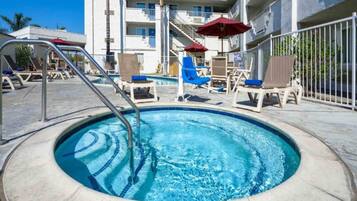 Une piscine entourée de chaises longues et de parasols, le tout bordé par un immeuble doté de nombreux balcons.