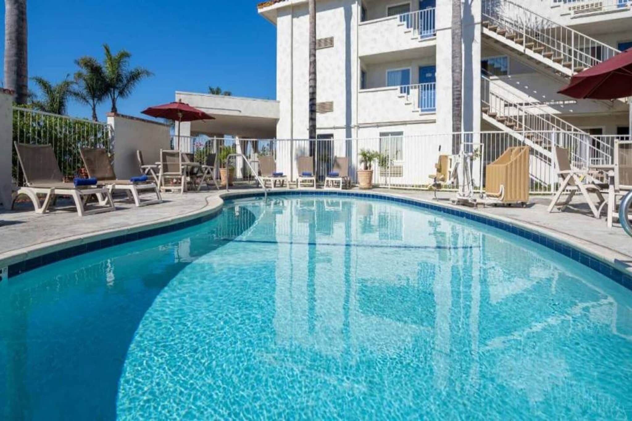 A swimming pool with lounge chairs and umbrellas, surrounded by a building with multiple balconies.