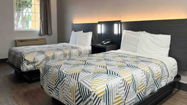 Ein Hotelzimmer mit zwei Betten, einem Nachttisch, einer Lampe und einem Fenster mit Vorhängen.