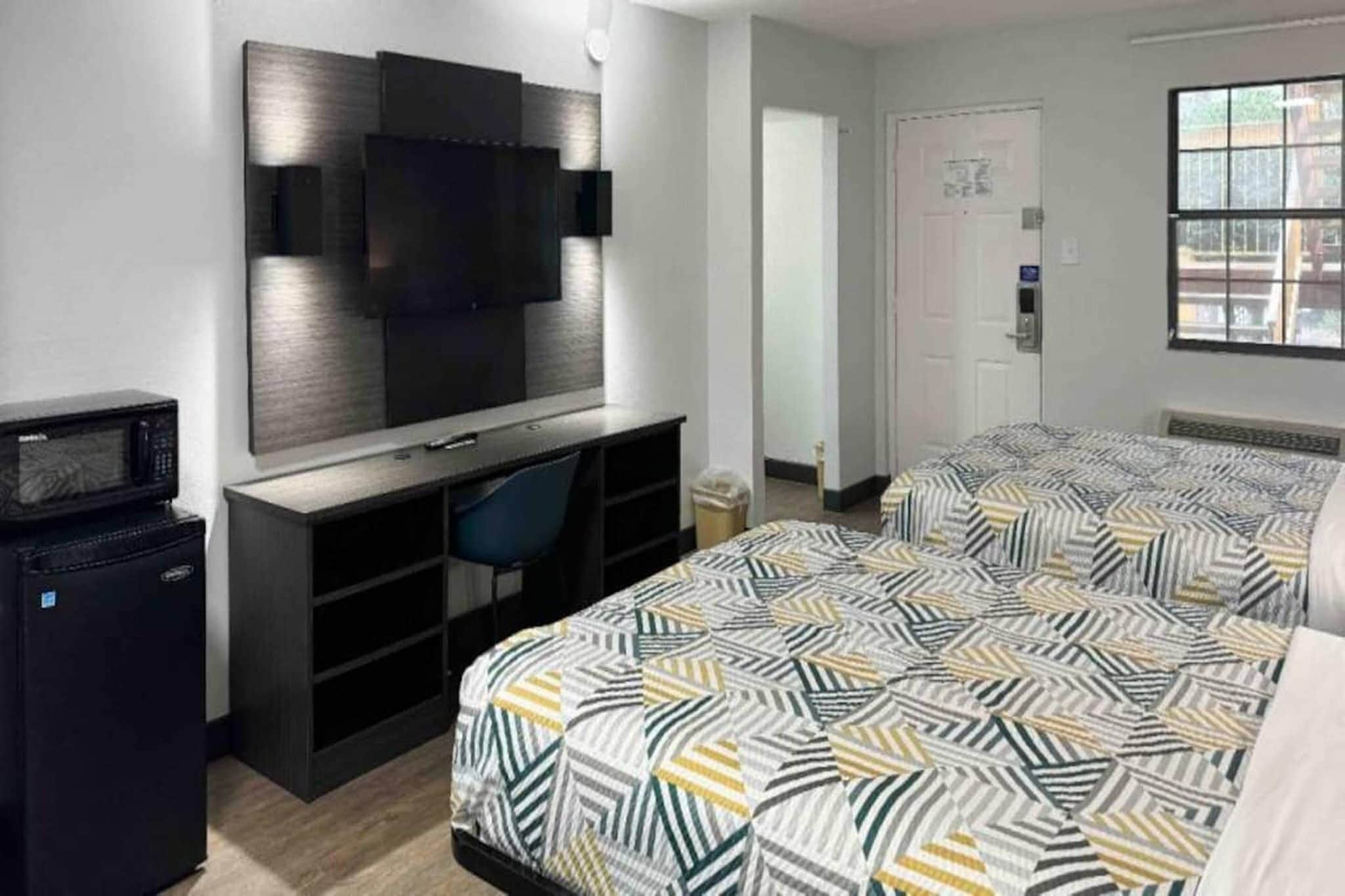 A hotel room with a bed, a desk with a chair, a television mounted on the wall, and a microwave.
