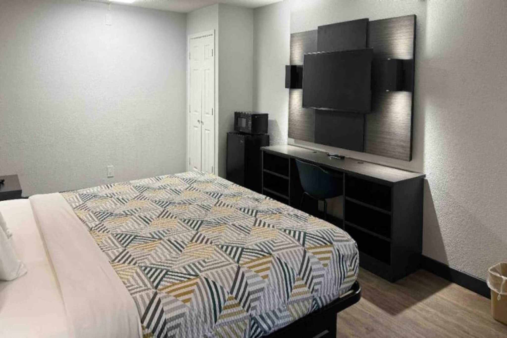 A hotel room with a bed, a desk, a chair, a television, and a wardrobe.