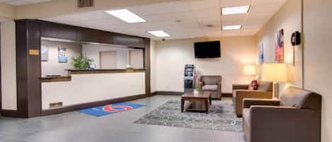 A hotel lobby with a reception desk, seating area, and a flat-screen TV mounted on the wall.