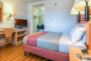 Ein Hotelzimmer mit Bett, Schreibtisch, Fernseher und einem durchgegangenen Tür sichtbaren Badezimmer.
