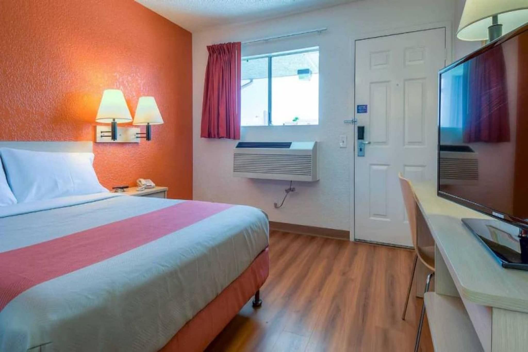 Une chambre d’hôtel comprenant un lit, des lampes de chevet, un bureau, une chaise, une télévision, un appareil de climatisation et une fenêtre avec des rideaux.