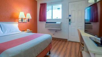 Une chambre d’hôtel comprenant un lit, des lampes de chevet, un bureau, une chaise, une télévision, un appareil de climatisation et une fenêtre avec des rideaux.