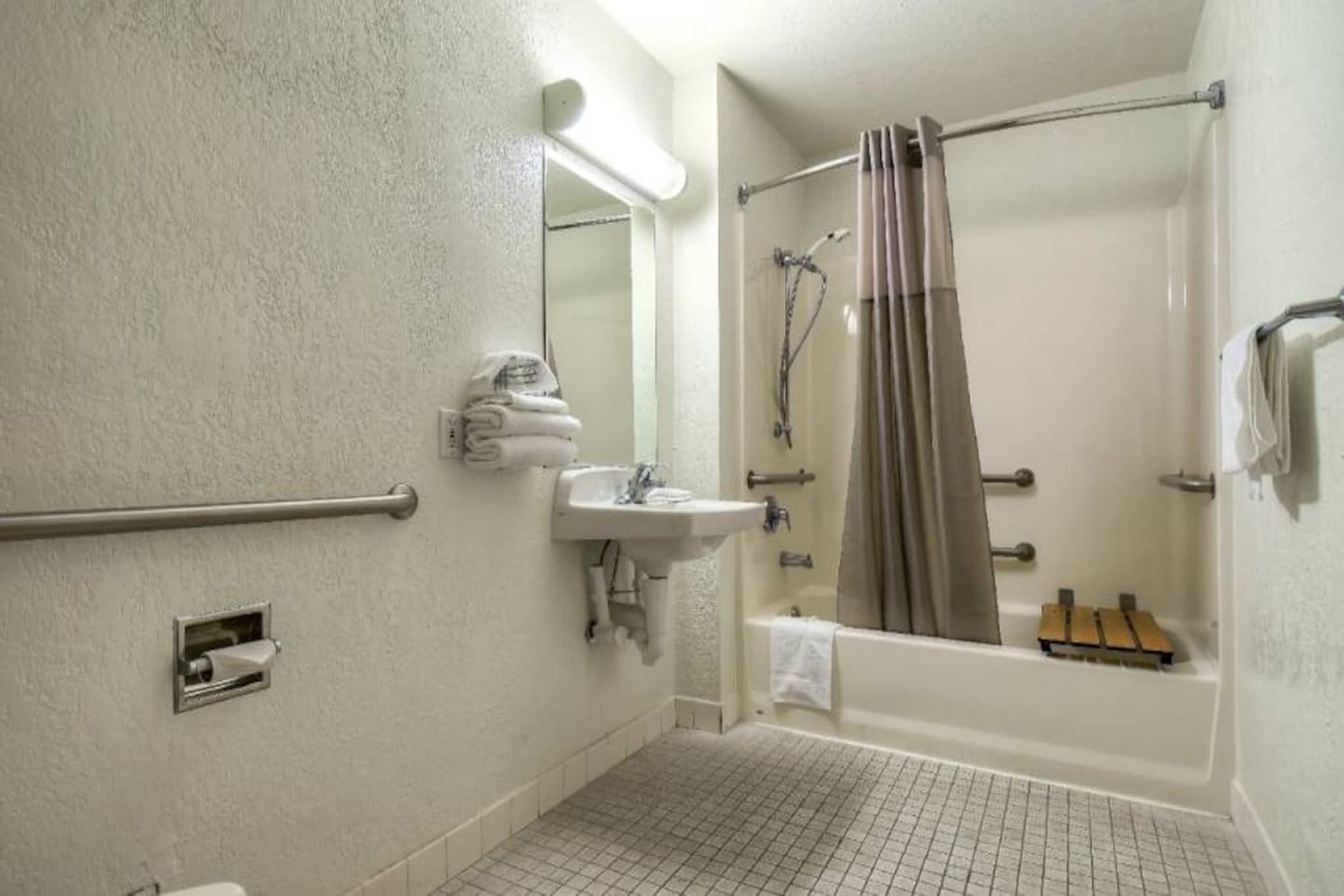 Un baño con ducha, lavamanos y barras de apoyo.
