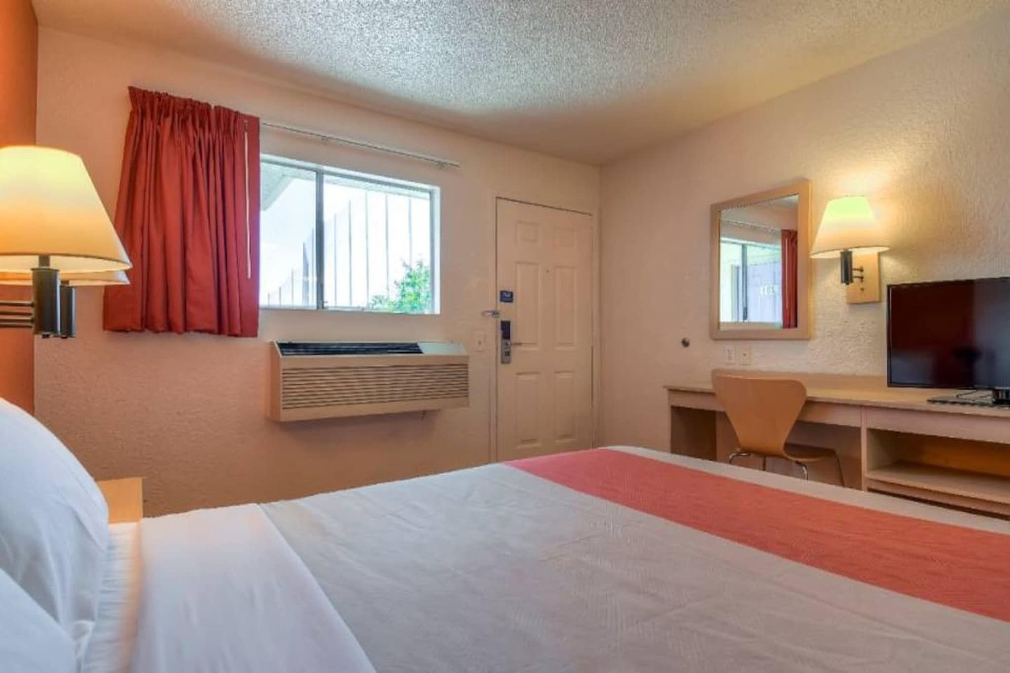 Una habitación de hotel con cama, escritorio con silla, televisor y ventana con cortinas.