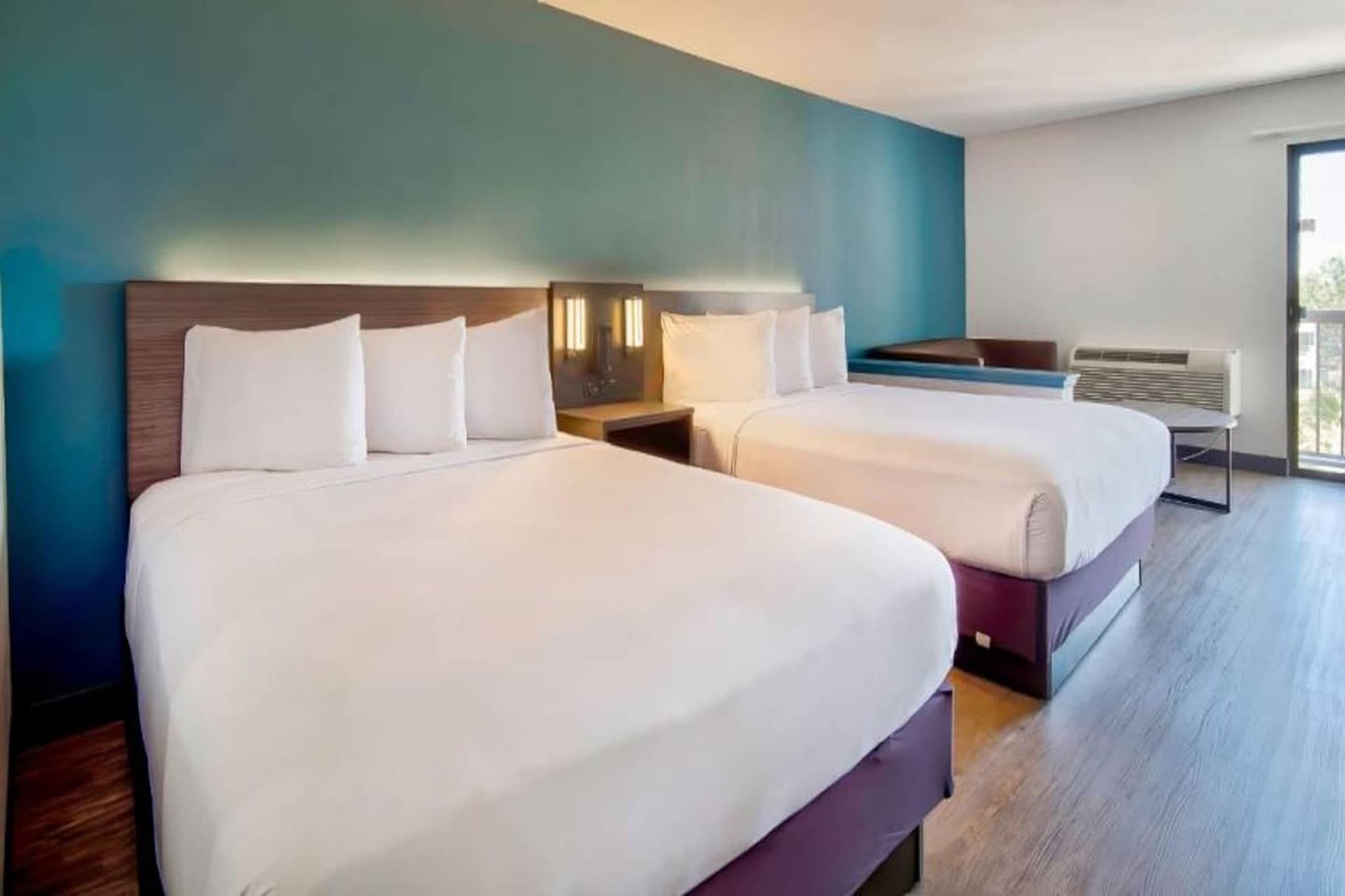 A hotel room with two beds, a nightstand, a desk, and a window.