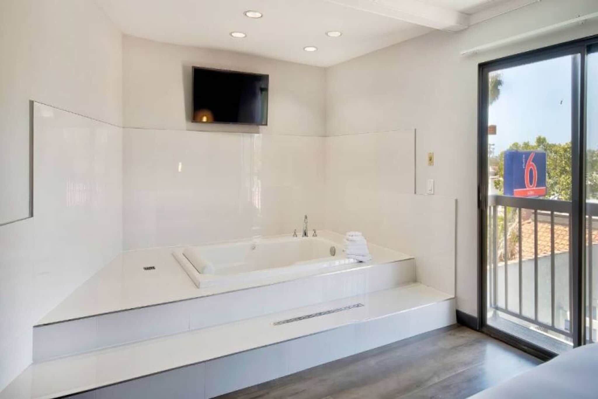 A modern bathroom with a large bathtub, a built-in TV, and a balcony with a view.