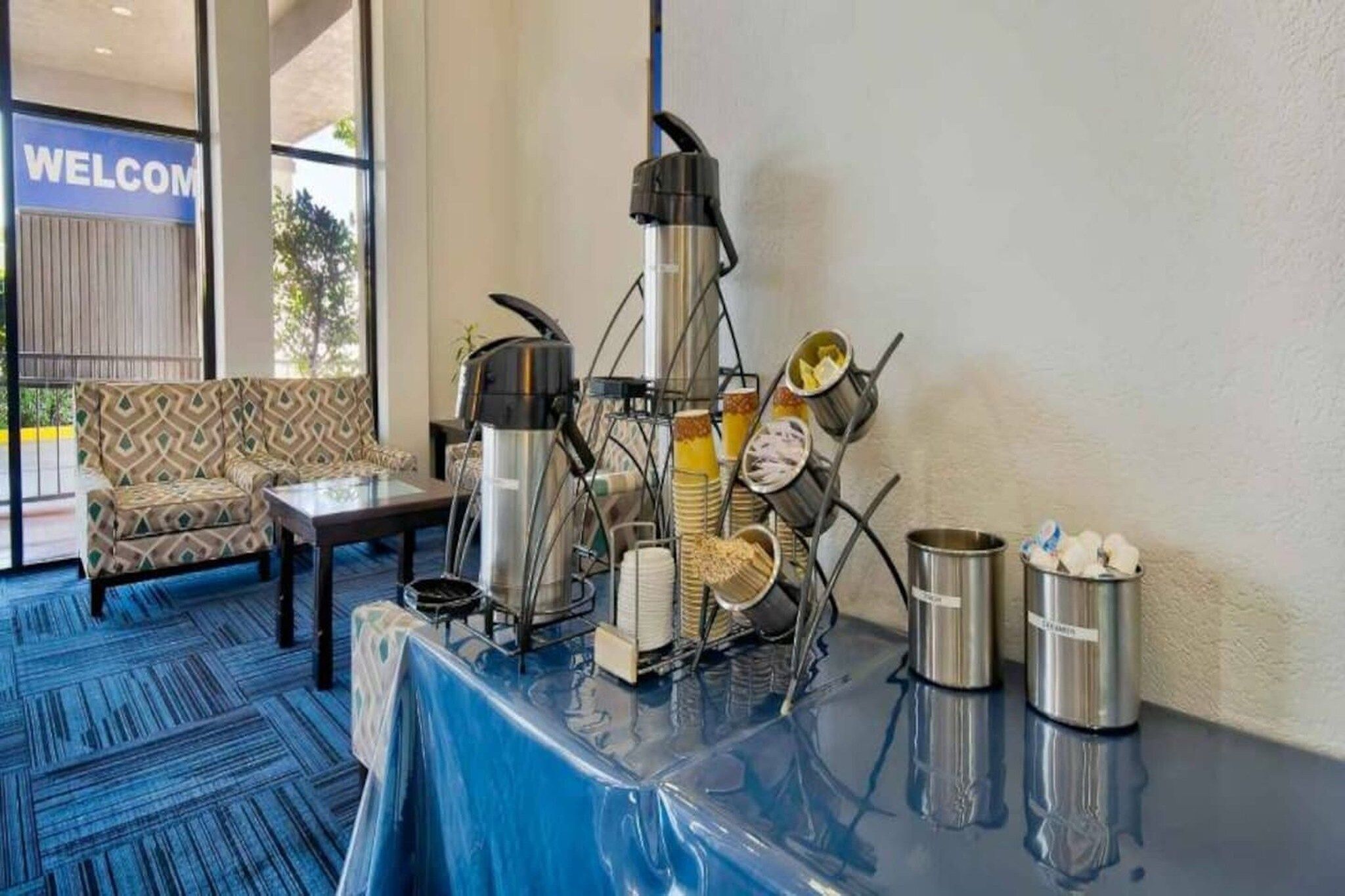 Ein Hotel-Rezeptionsbereich mit einer Kaffeestation, einer Couch und einem 'WELCOME'-Schild.