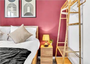 Une chambre à coucher avec un lit, une table de chevet, une lampe et un lit superposé en bois.