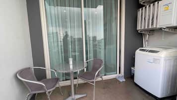 A small balcony with a glass door, two wicker chairs, a table, and a washing machine.