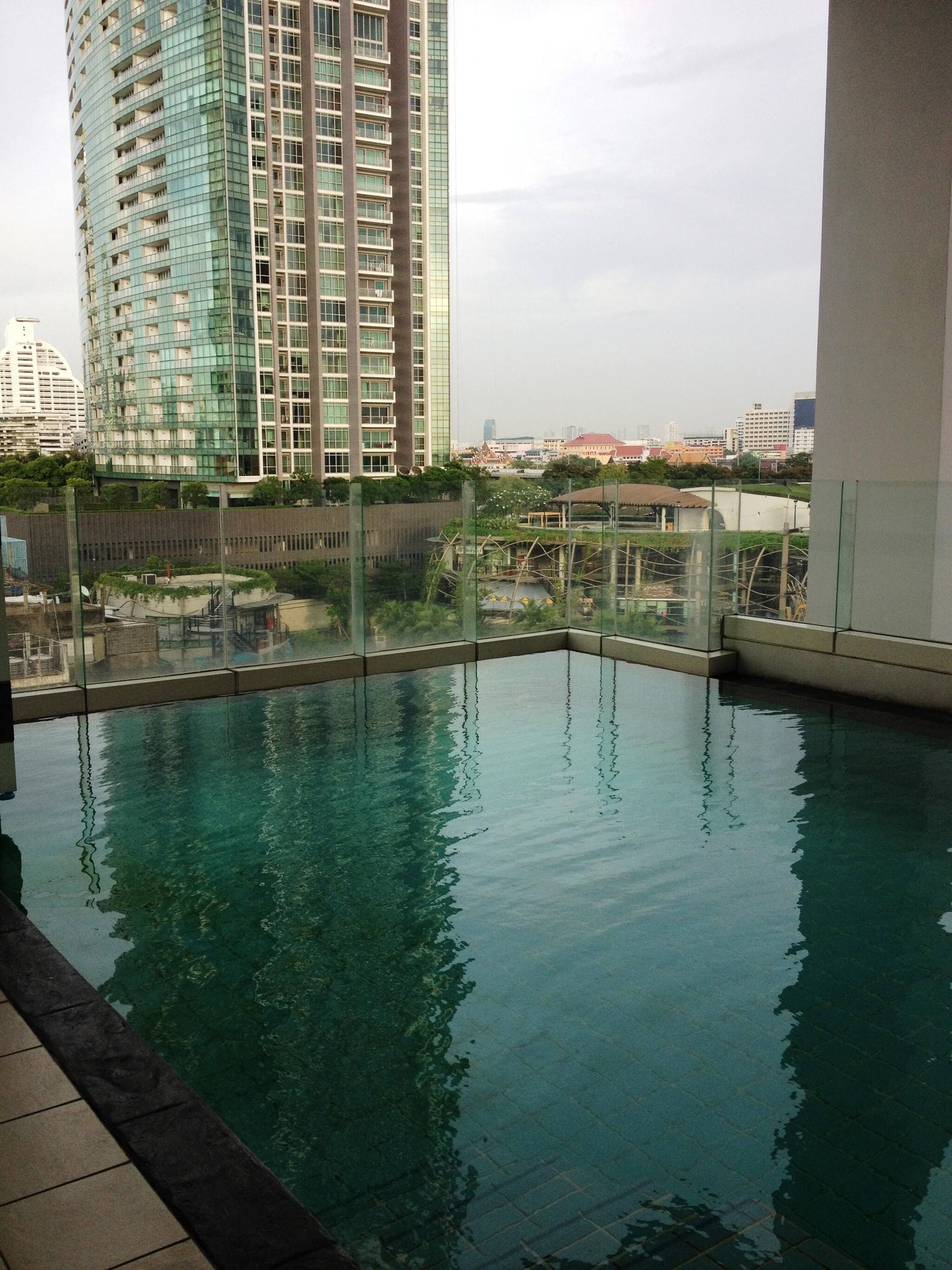 A rooftop swimming pool with a glass barrier, surrounded by high-rise buildings and a view of the cityscape.