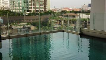 A rooftop swimming pool with a glass barrier, surrounded by high-rise buildings and a view of the cityscape.