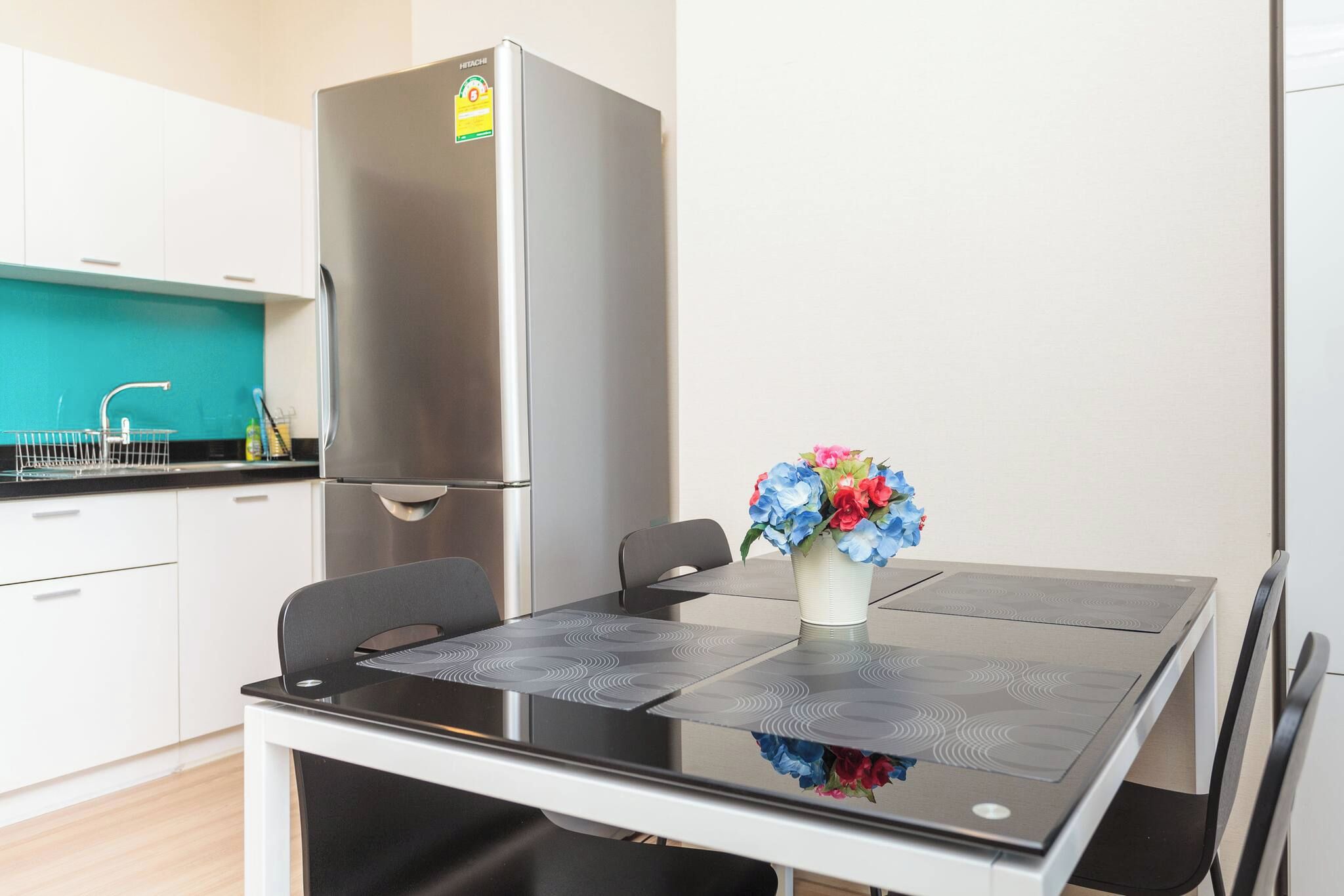 A modern kitchen with a stainless steel refrigerator, a dining table with chairs, and a vase with flowers.