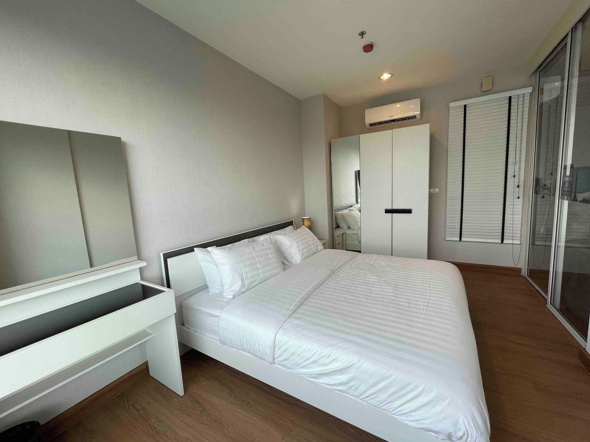 A modern bedroom with a bed, a desk, a wardrobe, and a sliding glass door.