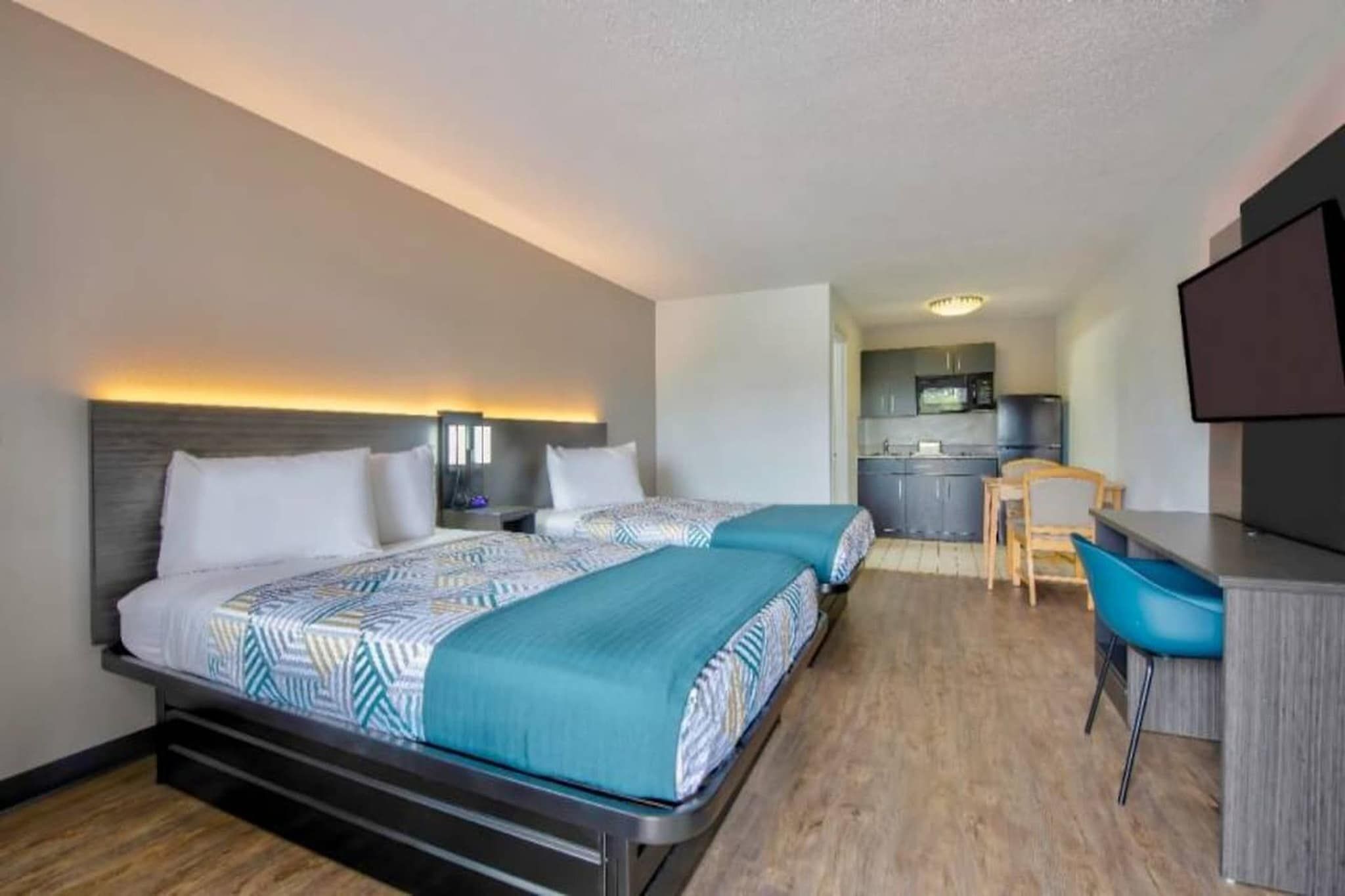 Habitación de hotel con dos camas, un escritorio, una silla, kitchenette y televisión.