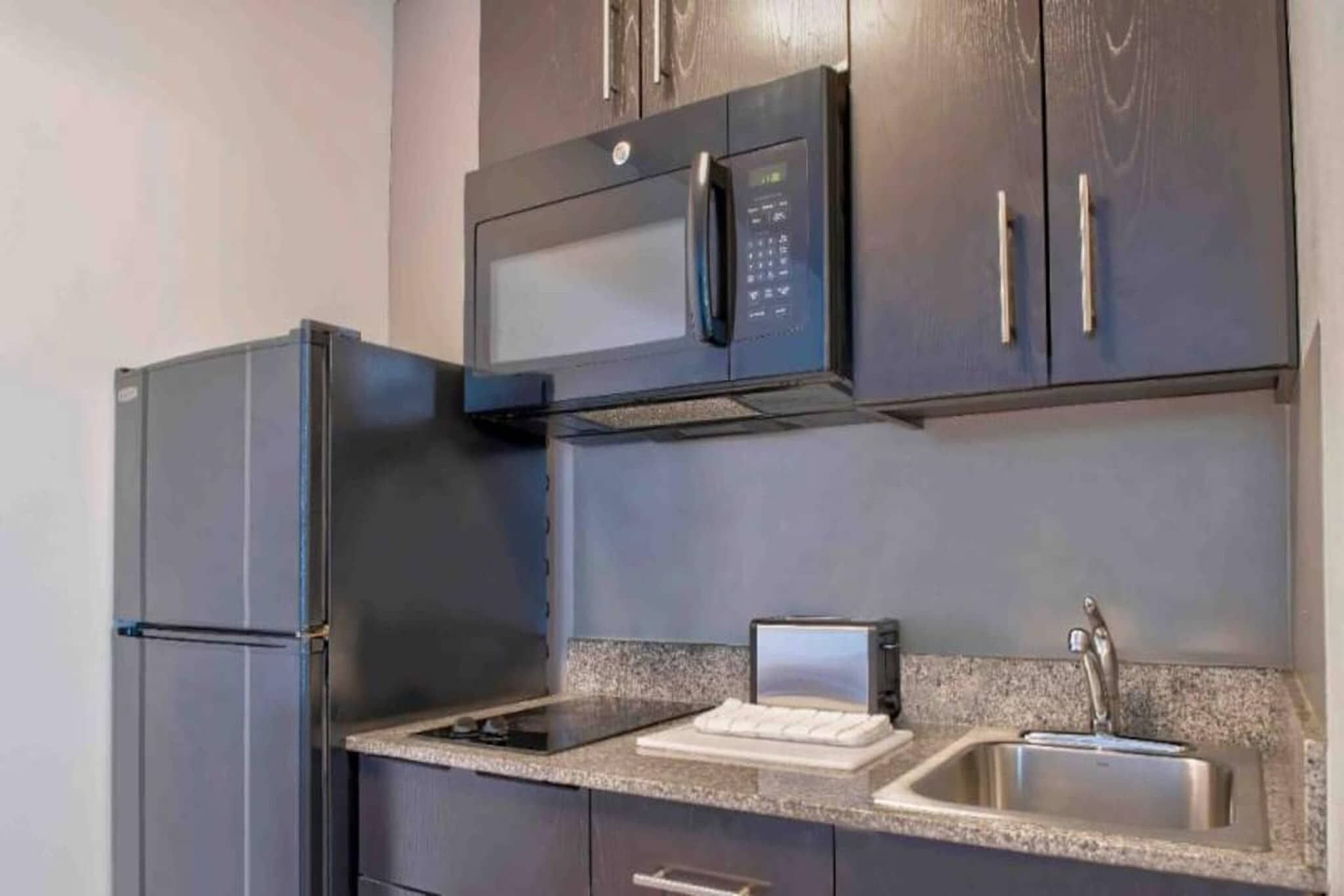 Una cocina moderna con microondas integrado, refrigerador, lavabo y encimera con una computadora portátil.
