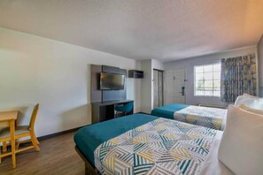 Quarto de hotel com duas camas, uma escrivaninha, televisão e janela com cortinas.