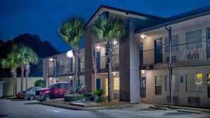 A multi-story hotel with a parking lot, palm trees, and a red car parked outside. - 1 Queen Bed | Non-Smoking (Pascagoula)