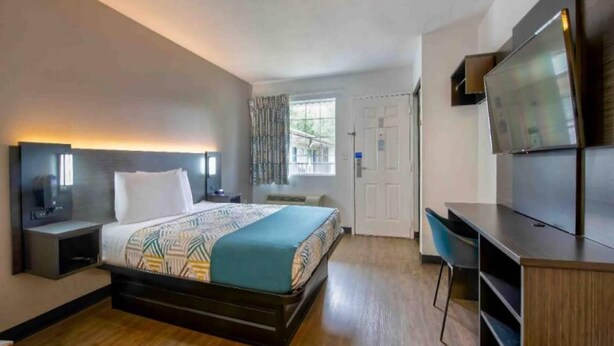 A hotel room with a bed, a desk, a chair, a TV, and a window with curtains. - 1 Queen Bed | Non-Smoking (Pascagoula)