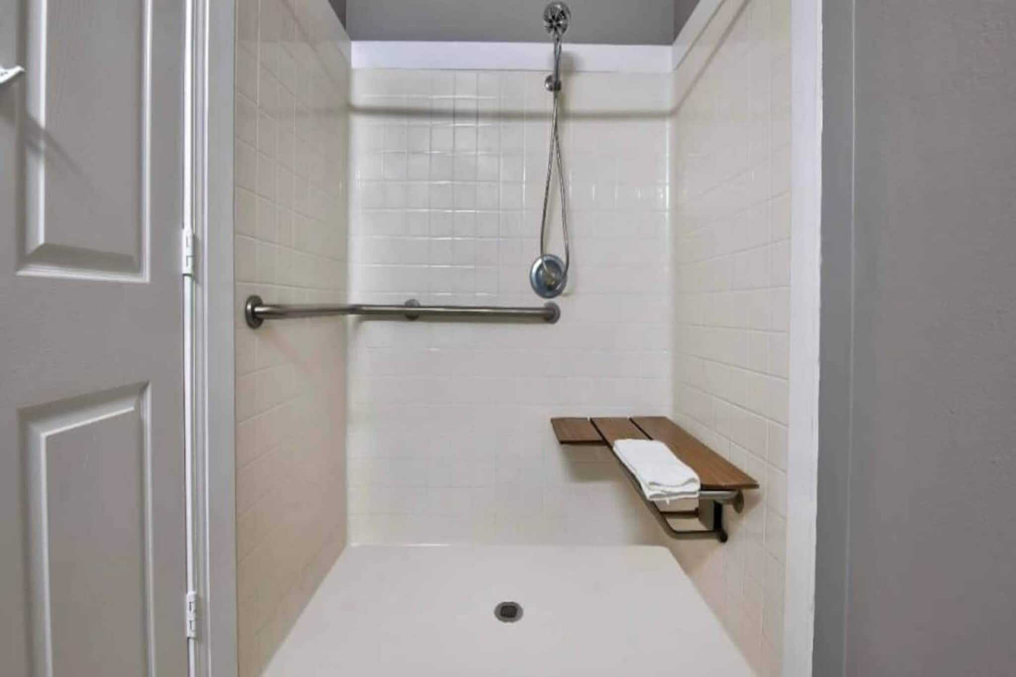 Une douche équipée d’un pommeau de douche à main, d’un porte-serviettes et d’un banc avec une serviette.