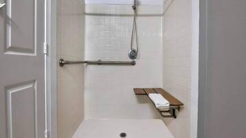 Une douche équipée d’un pommeau de douche à main, d’un porte-serviettes et d’un banc avec une serviette.