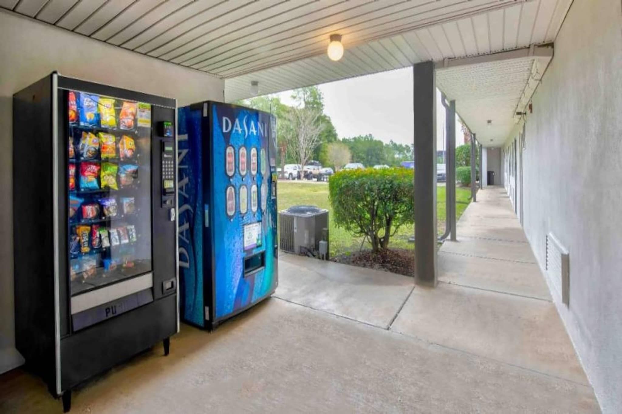 Una máquina expendedora y un quiosco de autoservicio bajo una zona cubierta, con suelo de hormigón y vistas al exterior.