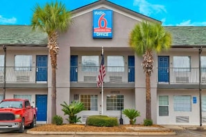 A 6 extended stay office building with a sign, two palm trees, an American flag, and a red truck parked in front.