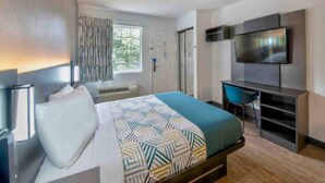 A modern hotel room with a bed, a desk, a television, and a window with curtains. - 1 Queen Bed | Non-Smoking (Pascagoula)