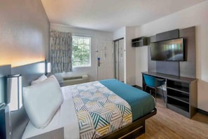 Ein modernes Hotelzimmer mit Bett, Schreibtisch, Fernseher und einem fenster mit Vorhängen.