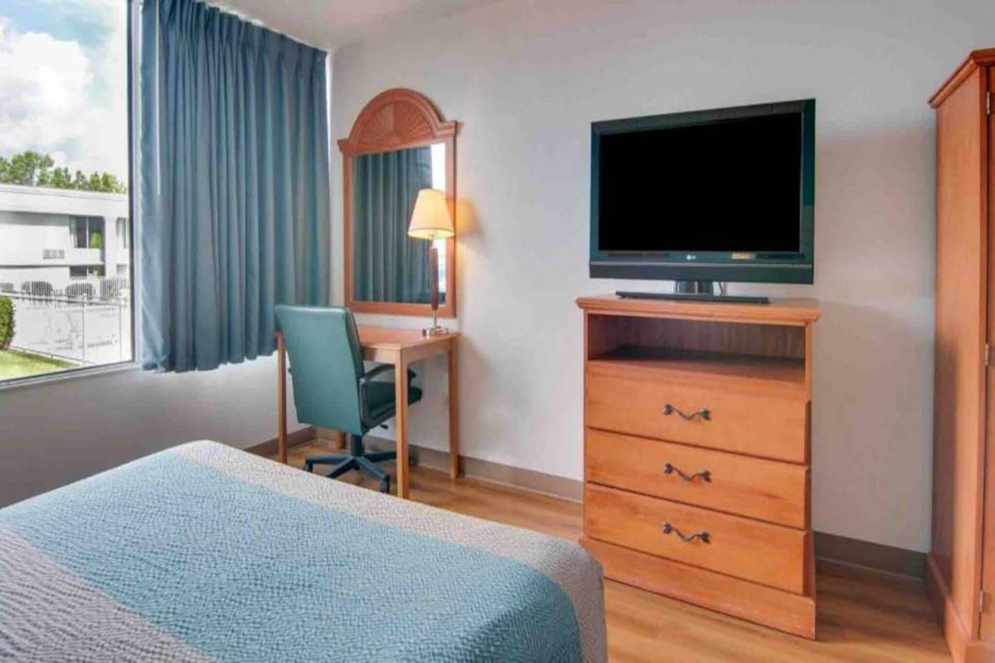 Una habitación de hotel con una cama, un escritorio con una silla, un televisor y un armario.