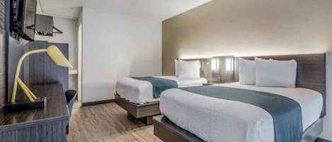 A hotel room with two beds, a desk, and a lamp.